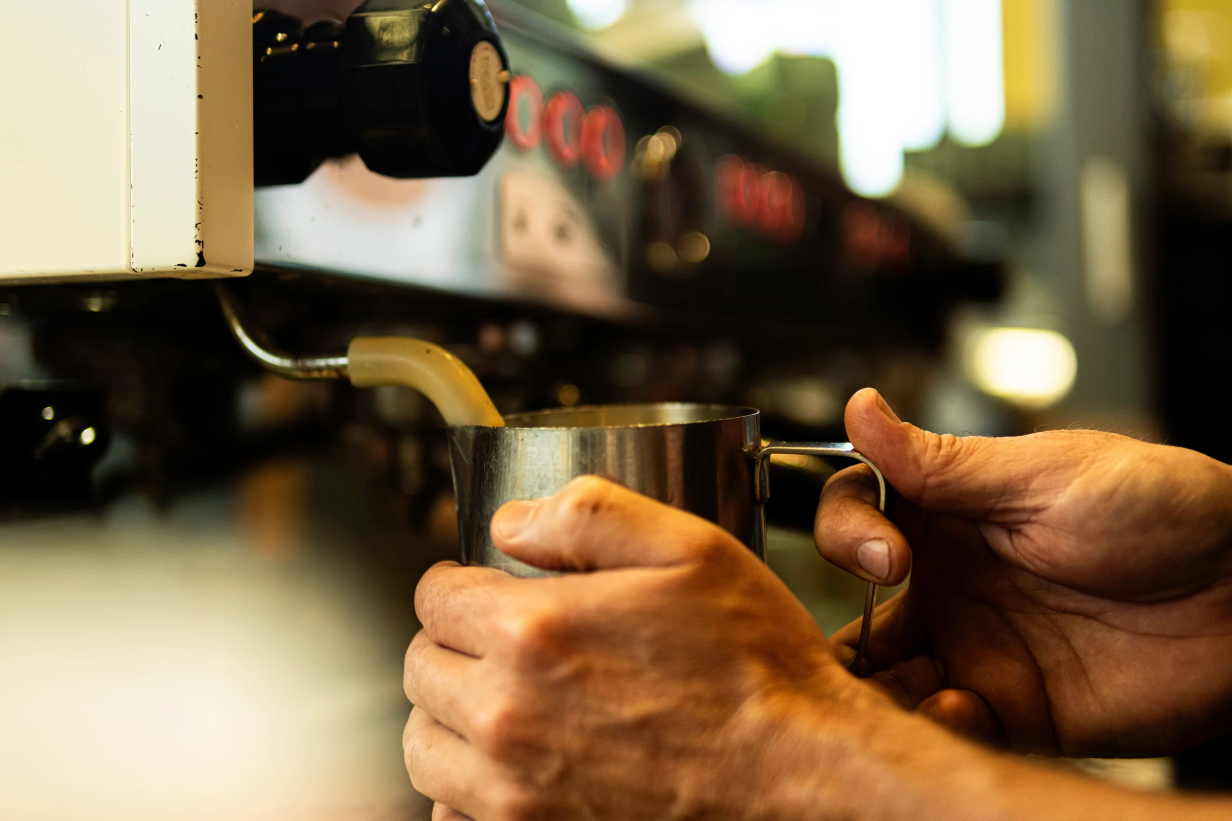 Hands steaming milk in a pitcher at an espresso machine