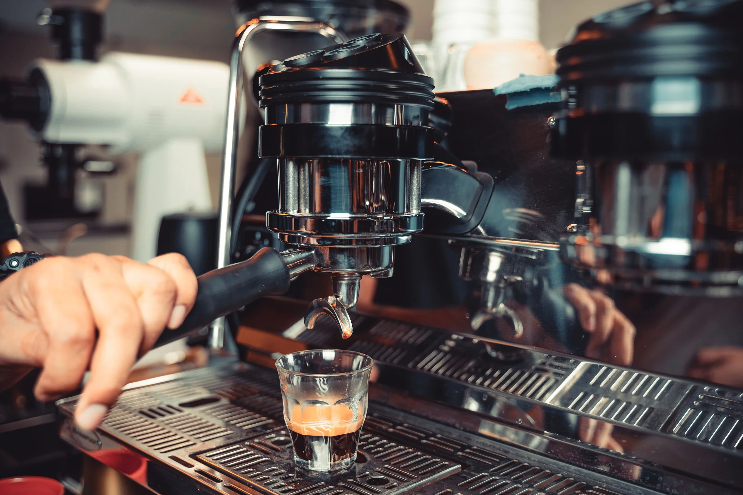 A barista pulling a shot of espresso into a small glass