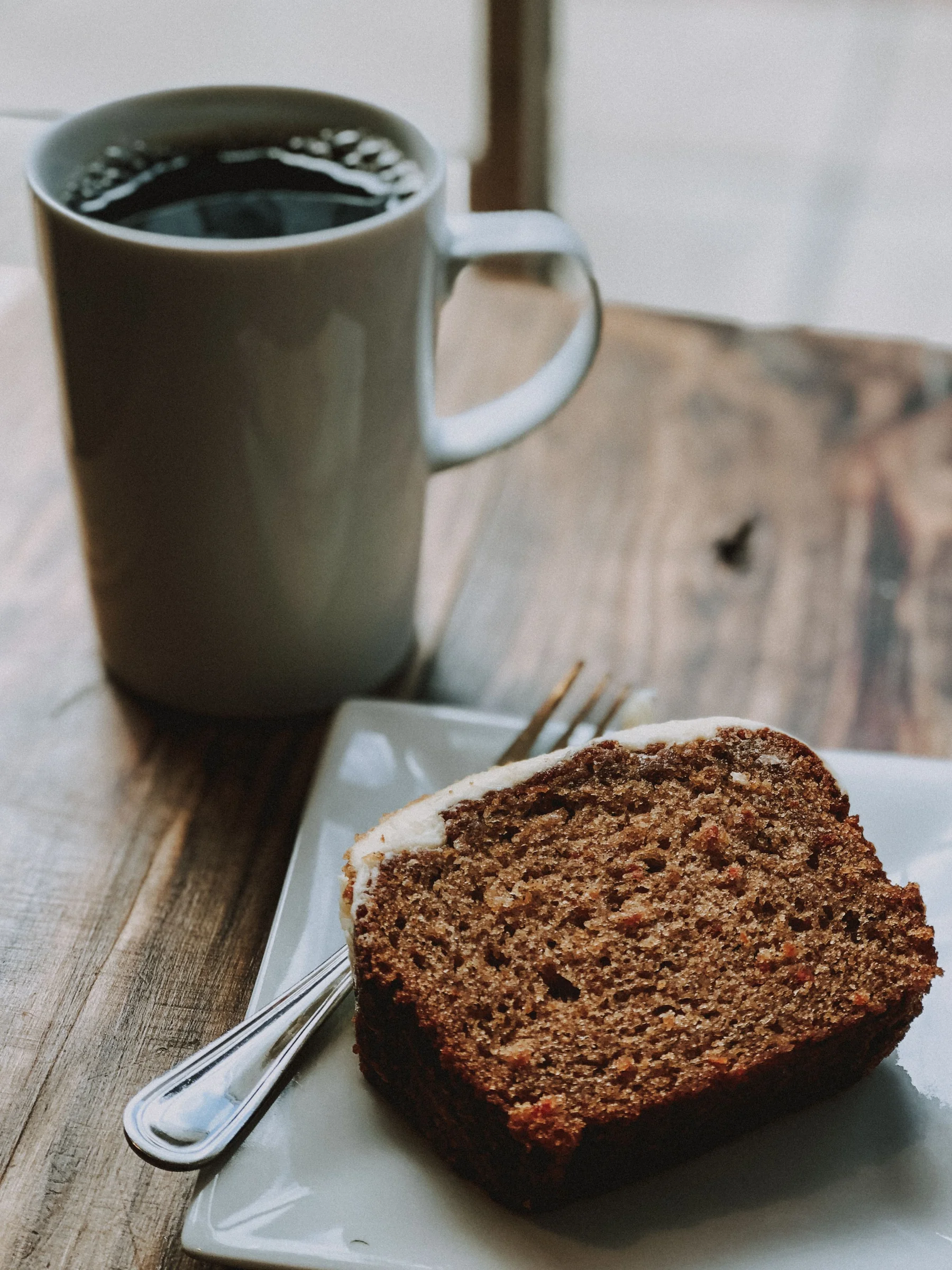 A slice of banana bread on a small plate beside a mug of coffee